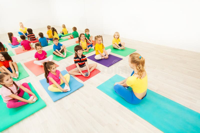 Group of sporty kids sitting on yoga mats and doing butterfly stretch with female instructor in exercise room. Group of sporty kids sitting on yoga mats and doing butterfly stretch with female instructor in exercise room