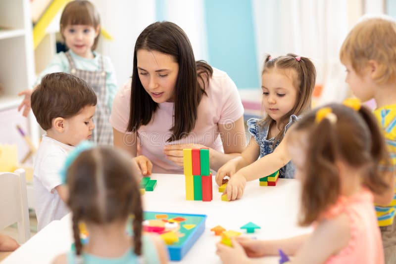 Bambini che giocano con i giocattoli educativi nell'asilo Insegnante della scuola materna che si occupa dei bambini immagini stock Bambini che giocano con i giocattoli educativi nell'asilo Insegnante della scuola materna che si occupa dei bambini immagini stock