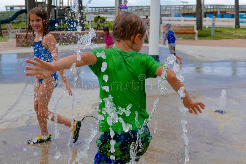 Bambini che giocano in una spruzzatrice d'acqua esterna immagini stock Bambini che giocano in una spruzzatrice d'acqua esterna immagini stock