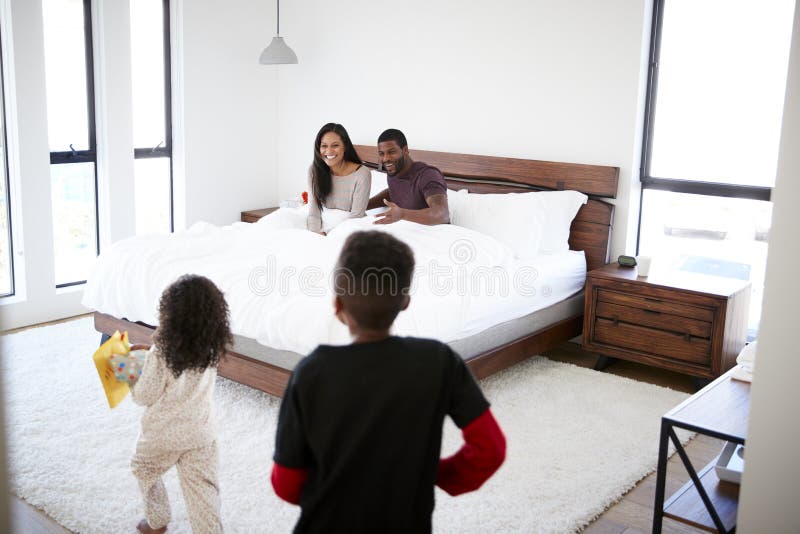 Bambini che si imbattono nella camera da letto dei genitori con il regalo e la carta a letto per celebrare giorno o compleanno di fotografie stock libere da diritti Bambini che si imbattono nella camera da letto dei genitori con il regalo e la carta a letto per celebrare giorno o compleanno di fotografie stock libere da diritti
