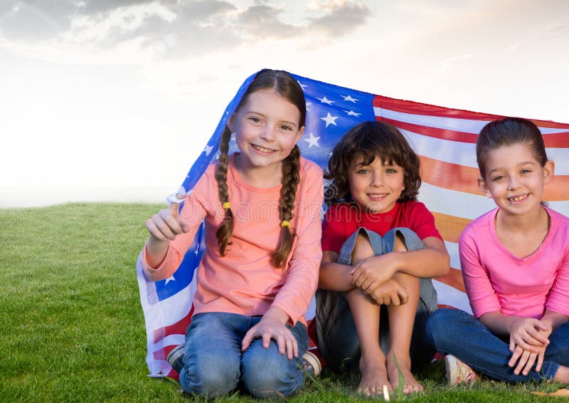 Bambini che si siedono sotto le bandiere americane nel campo fotografie stock Bambini che si siedono sotto le bandiere americane nel campo fotografie stock