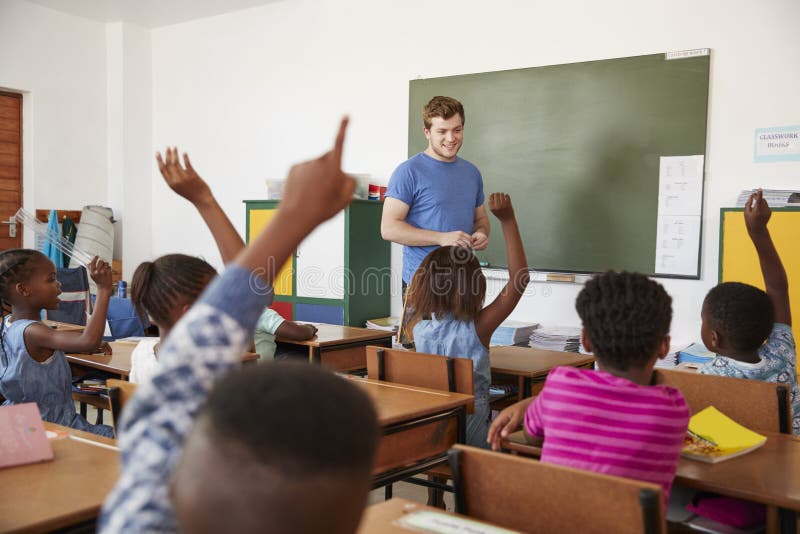 Bambini che sollevano le mani all'insegnante in una classe della scuola elementare fotografie stock libere da diritti Bambini che sollevano le mani all'insegnante in una classe della scuola elementare fotografie stock libere da diritti