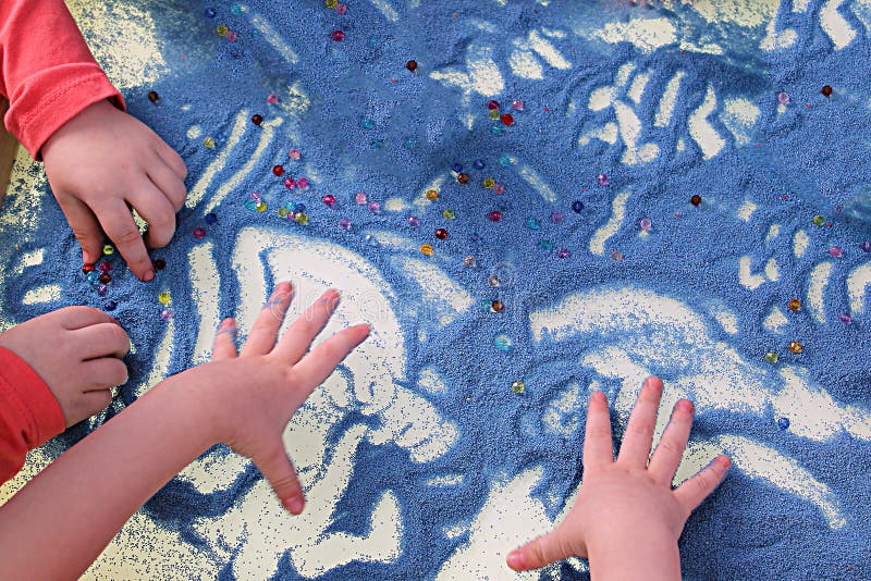 Childrens hands touching blue sand on white table, sand therapy, development of fine motor skills. Childrens hands touching blue sand on white table, sand therapy, development of fine motor skills