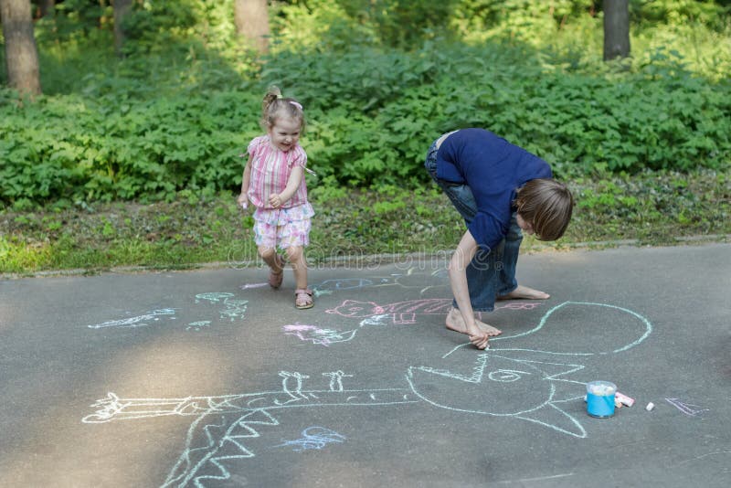 Bambini del fratello germano divertendosi durante il marciapiede che segna sulla superficie dell'asfalto immagine stock Bambini del fratello germano divertendosi durante il marciapiede che segna sulla superficie dell'asfalto immagine stock