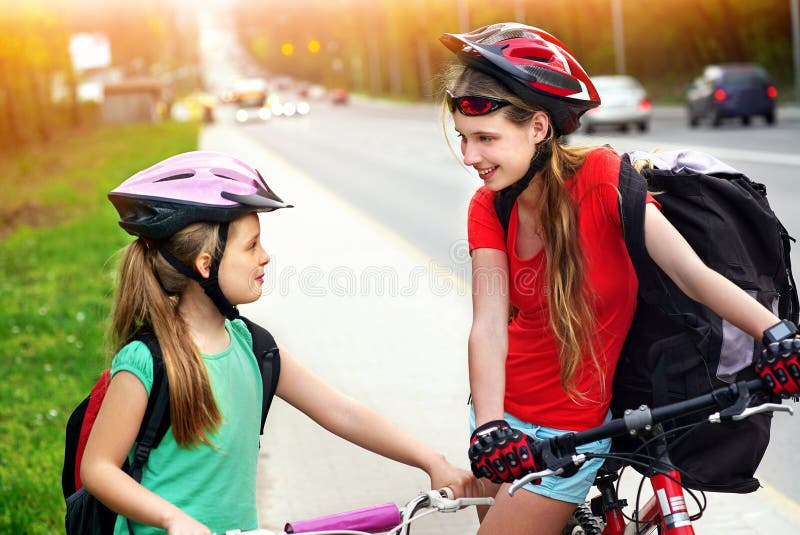 Bambini delle ragazze che ciclano sul vicolo giallo della bici Ci sono automobili sulla strada fotografia stock Bambini delle ragazze che ciclano sul vicolo giallo della bici Ci sono automobili sulla strada fotografia stock