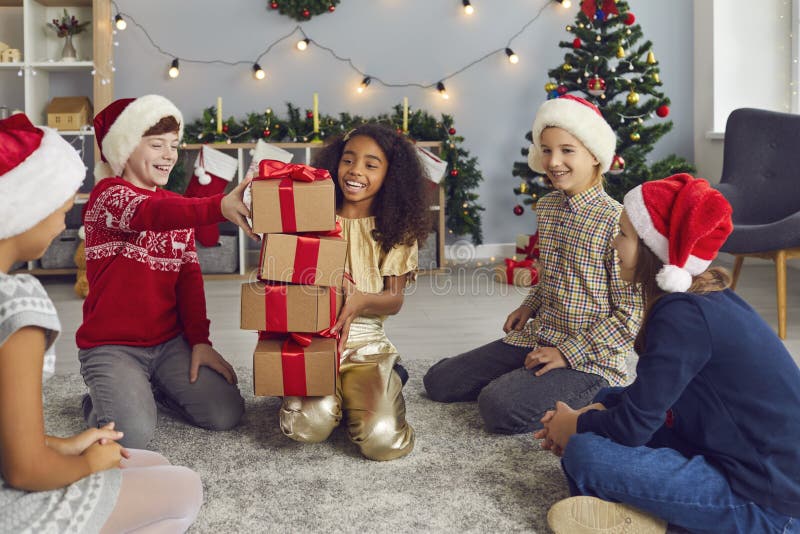 Bambini di razza mista sorridenti seduti sul pavimento e raccolgono un mucchio di scatole regalo a casa durante il Natale fotografia stock