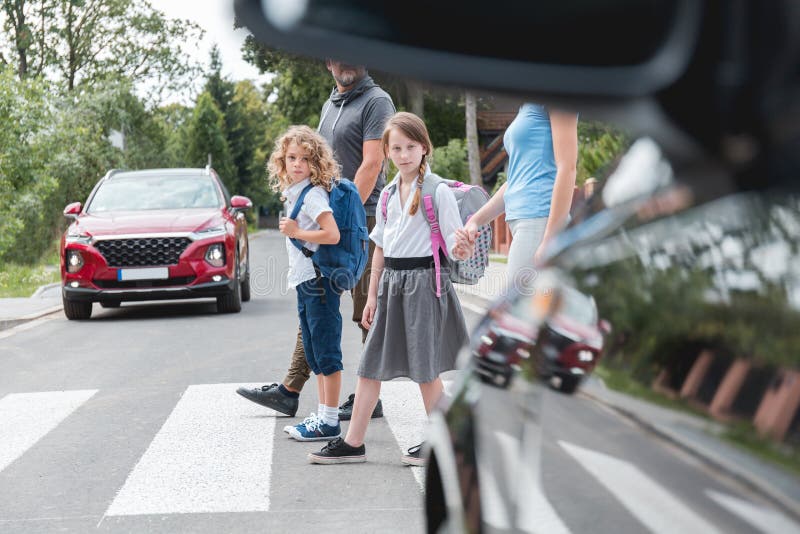 Bambini in età scolare attraversano la strada pedonale proprio di fronte alla macchina fotografia stock libera da diritti