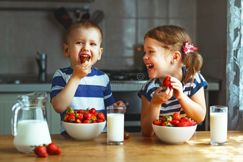 Bambini felici fratello e sorella che mangiano le fragole con latte