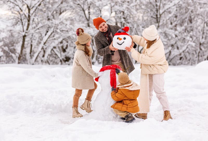 Bambini felici scolpiscono un pupazzo di neve divertente insieme ai genitori nel parco coperto di neve invernale