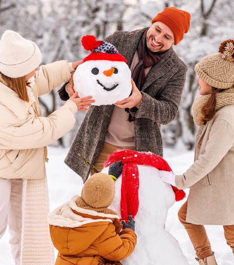 Bambini felici scolpiscono un pupazzo di neve divertente insieme ai genitori nel parco coperto di neve invernale