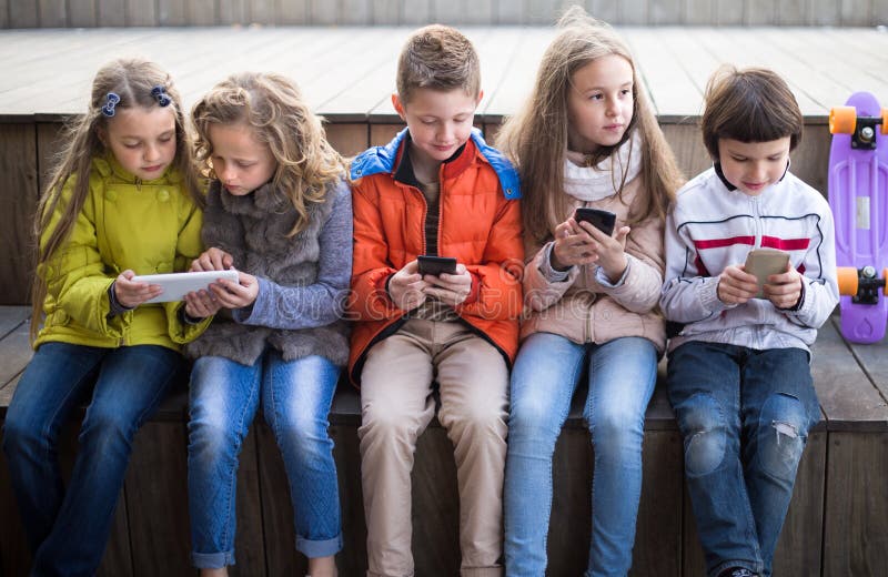 Bambini ordinari che giocano con il telefono sul banco all'aperto fotografia stock Bambini ordinari che giocano con il telefono sul banco all'aperto fotografia stock