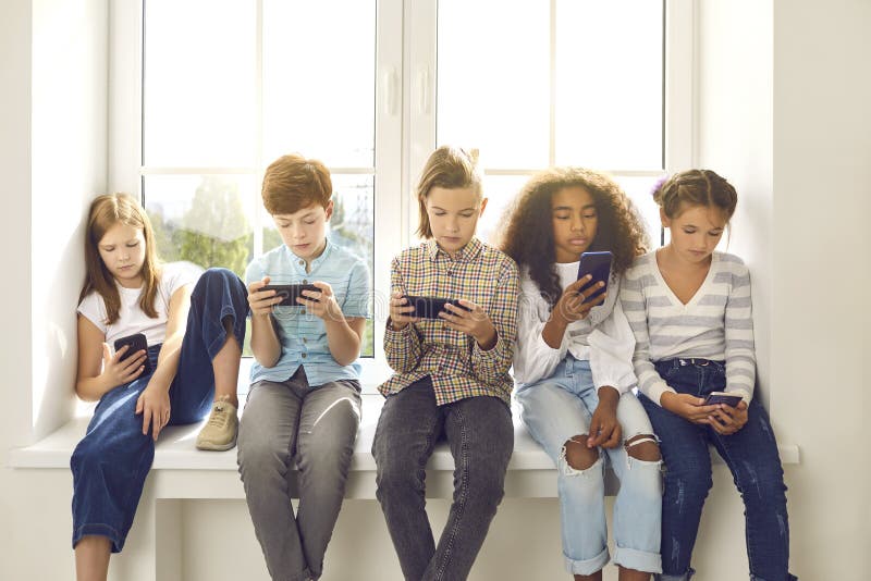 Bambini seduti su una finestra giocano a giochi online sui telefoni cellulari e si ignorano a vicenda immagine stock libera da diritti