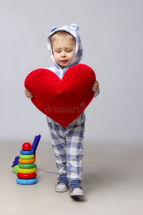 Bambino affascinante che tiene un cuore rosso in mani immagine stock libera da diritti Bambino affascinante che tiene un cuore rosso in mani immagine stock libera da diritti