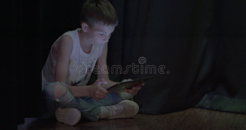 Bambino affaticato per gli occhi gioca a giochi per computer sulla tavoletta al buio. messa a fuoco sullo schermo.