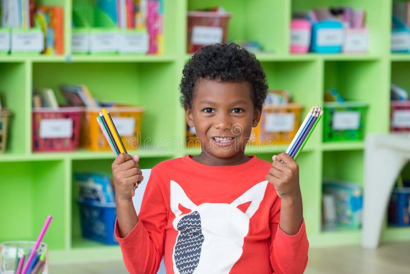 Bambino afroamericano di etnia che tiene gruppo di SMI della matita di colore immagine stock Bambino afroamericano di etnia che tiene gruppo di SMI della matita di colore immagine stock