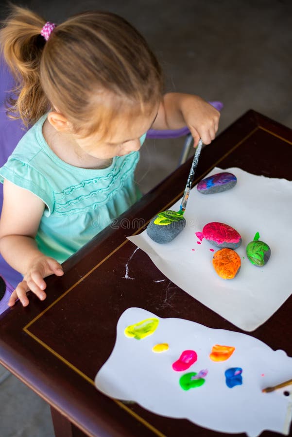 Bambino in camicia da tè dipinge pietre colorate con un'attività artistica per un bambino piccolo o più piccolo