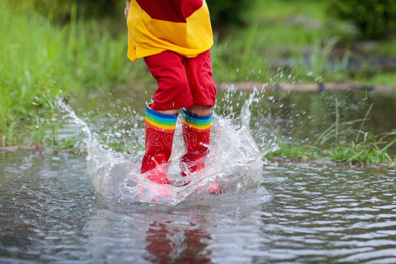 Bambino che gioca fuori nella pioggia Bambini con gli stivali di pioggia e dell'ombrello giocare all'aperto in pioggia persistent
