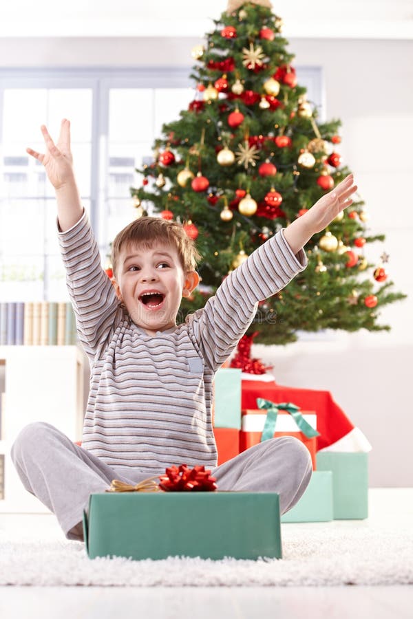 Kid yelling happily at christmas gift with arms raised, sitting at christmas tree in morning. Kid yelling happily at christmas gift with arms raised, sitting at christmas tree in morning.