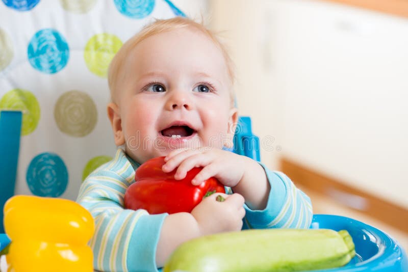 Bambino con le verdure che si siedono nella sedia sulla cucina fotografia stock Bambino con le verdure che si siedono nella sedia sulla cucina fotografia stock