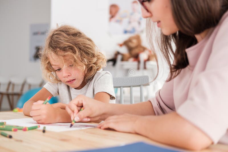Bambino con un disordine di spettro di autismo ed il terapista da un disegno della tavola con i pastelli durante il sensoriale Bambino con un disordine di spettro di autismo ed il terapista da un disegno della tavola con i pastelli durante il sensoriale