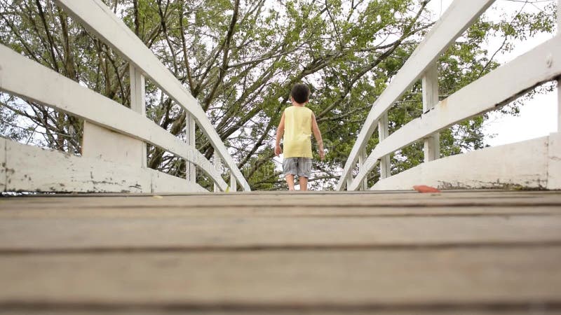 Bambino di 7 anni a piedi nudi camminando sul ponte curvo e guardando indietro