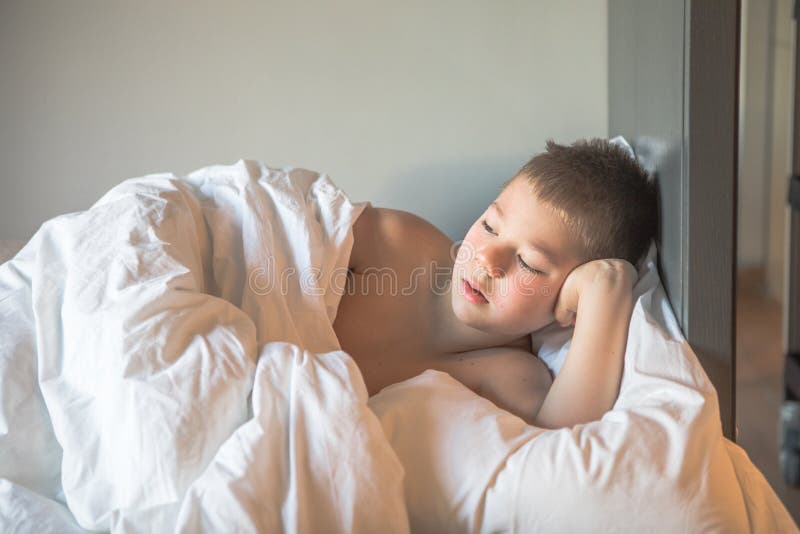 Bambino di 7 anni sdraiato sul letto, assonnato bambino che si sveglia la mattina nel suo letto con un bambino triste e leggero ch fotografie stock