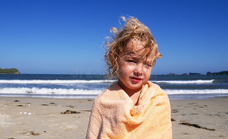 Bambino di colore medio e carino con capelli biondi ricci che si sentono freddi sulla spiaggia che si riscaldano con un asciugaman immagini stock libere da diritti