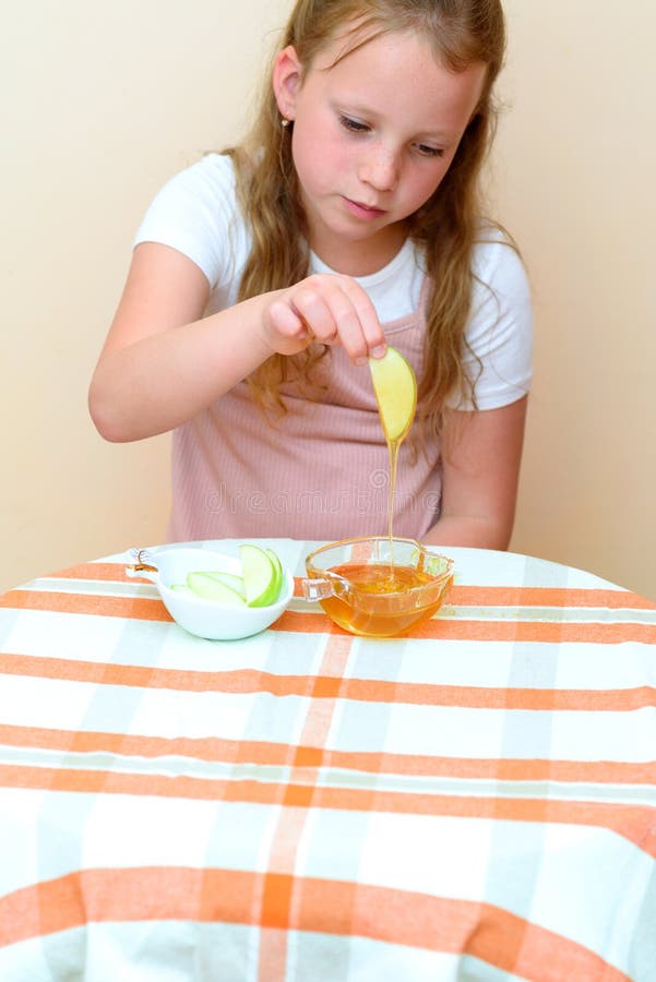 Bambino ebreo che immerge le fette della mela nel miele su Rosh HaShanah fotografia stock Bambino ebreo che immerge le fette della mela nel miele su Rosh HaShanah fotografia stock