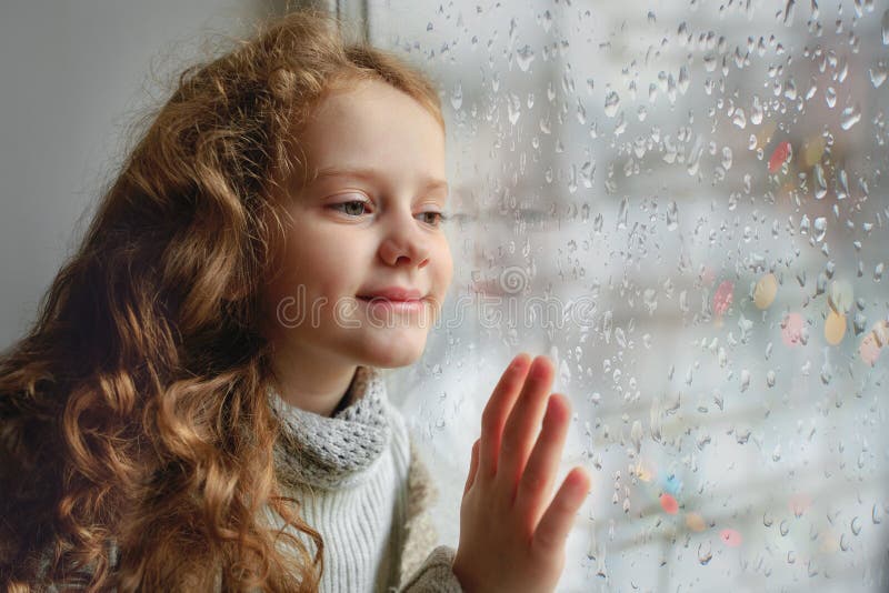 Bambino felice che guarda fuori la finestra con il wea di vetro bagnato di Male di autunno fotografia stock libera da diritti Bambino felice che guarda fuori la finestra con il wea di vetro bagnato di Male di autunno fotografia stock libera da diritti