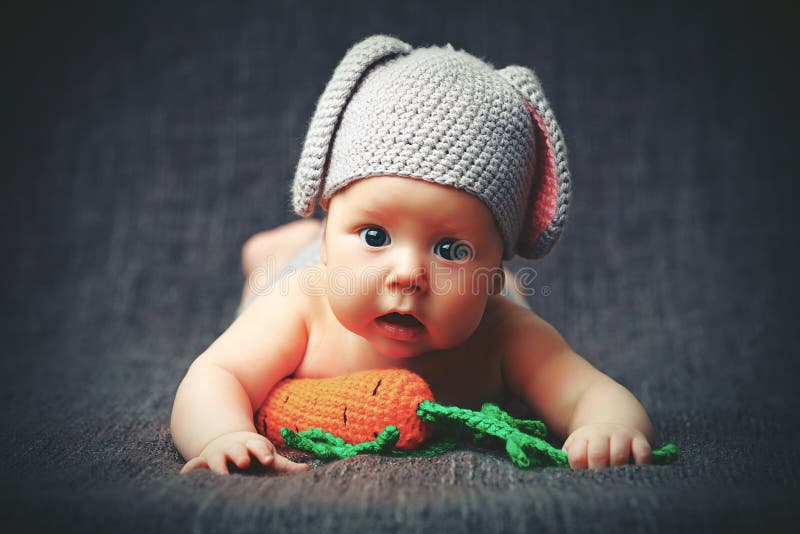 Bambino felice del bambino in costume un coniglietto del coniglio con la carota su un grey fotografia stock