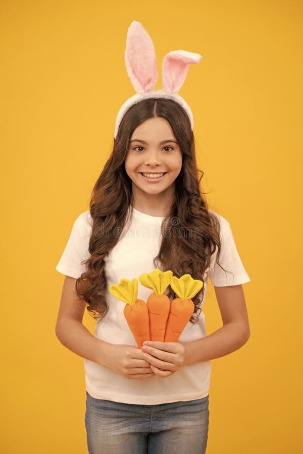 Bambino felice nelle orecchie di coniglio tiene la carota sulla pasqua gialla fotografie stock
