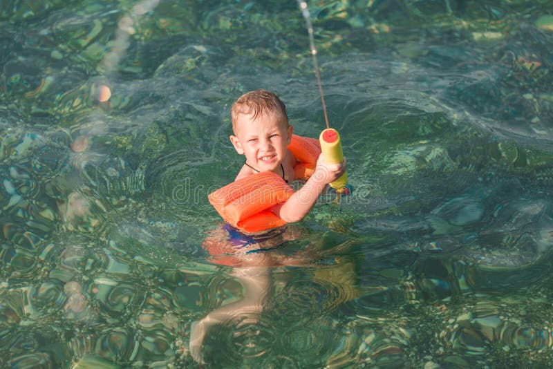 Bambino felice sveglio che gioca con la pistola di acqua fotografia stock libera da diritti Bambino felice sveglio che gioca con la pistola di acqua fotografia stock libera da diritti