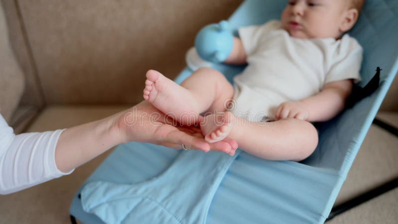 Bambino giace nella sala chaise con un suono in mano che la mamma tiene il neonato per gambe. concetto di maternità stock footage
