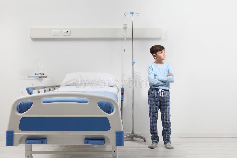 Bambino in ospedale seduto accanto al letto con un pajama isolato sul muro bianco