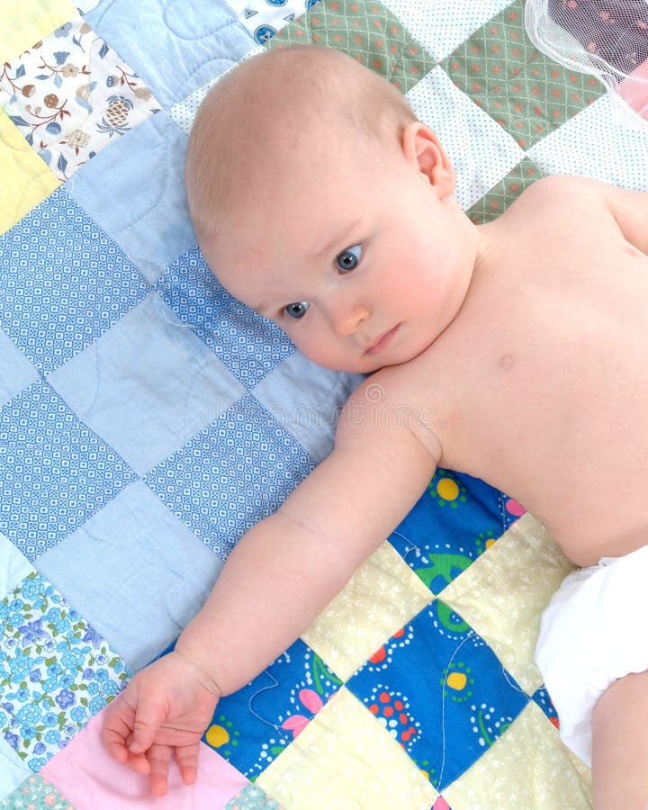 Cute baby lying on back on a multicolored quilt with arm extended. Cute baby lying on back on a multicolored quilt with arm extended