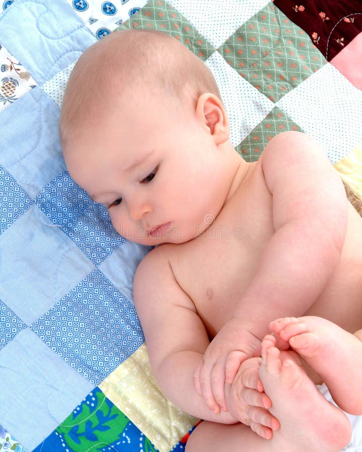 Cute baby lying on back on a multicolored quilt while holding his feet. Cute baby lying on back on a multicolored quilt while holding his feet