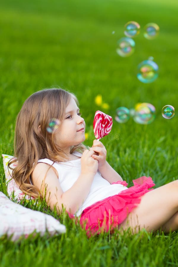 Bambino sveglio con il lollipop che riposa sull'erba immagini stock libere da diritti Bambino sveglio con il lollipop che riposa sull'erba immagini stock libere da diritti