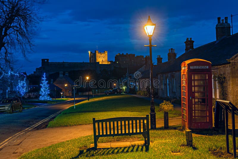 Bamburgh village, Northumberland, England, UK, at dusk, with Bamburgh Castle in the background, at Christmas. Bamburgh village, Northumberland, England, UK, at dusk, with Bamburgh Castle in the background, at Christmas