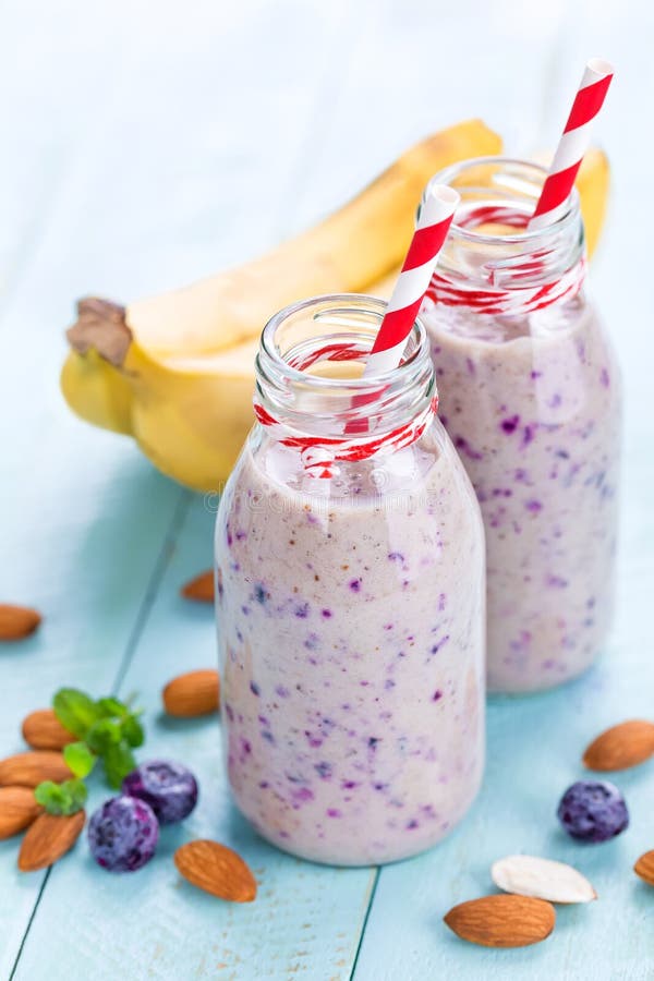 A banana e o mirtilo fazem dieta o batido com iogurte ou ordenham-no, amêndoas e bagas frescas nas garrafas de vidro foto de stock royalty free A banana e o mirtilo fazem dieta o batido com iogurte ou ordenham-no, amêndoas e bagas frescas nas garrafas de vidro foto de stock royalty free