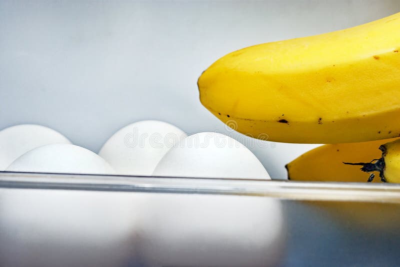 Bananfingrar och fyra vita ägg i plast- behållare för öppen kylskåpdörr Viktförlust bantar, sund organisk mat och royaltyfri bild Bananfingrar och fyra vita ägg i plast- behållare för öppen kylskåpdörr Viktförlust bantar, sund organisk mat och royaltyfri bild