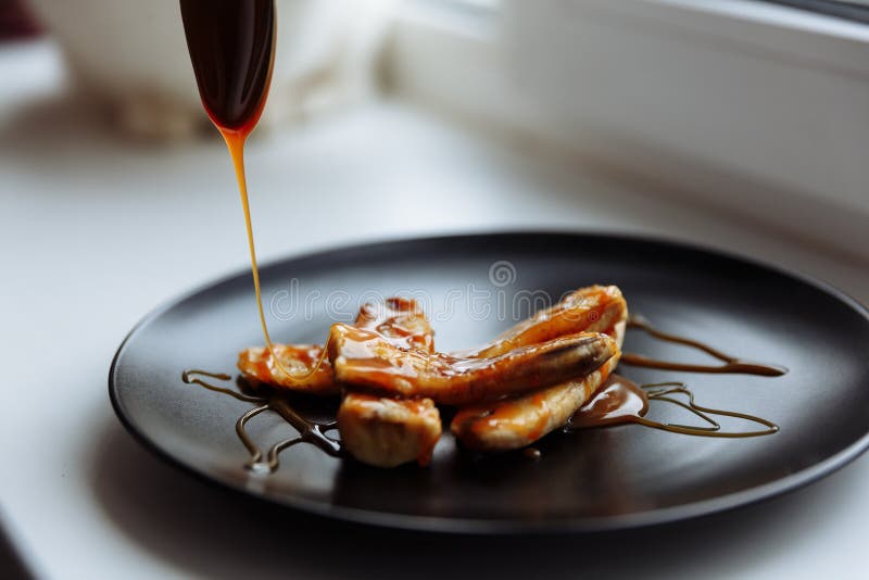 Banană caramelizată artizanală în plăci negre pe masă albă Desert vegetarian. concentrare selectivă stock image