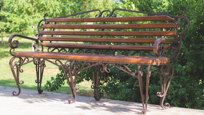 Banco de madera con el arte del metal que forja en el parque de atracciones Banco de Brown en el fondo verde de la naturaleza foto de archivo libre de regalías Banco de madera con el arte del metal que forja en el parque de atracciones Banco de Brown en el fondo verde de la naturaleza foto de archivo libre de regalías