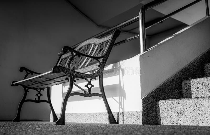 Banco vacío del hierro labrado colocado cerca de las escaleras del edificio Sol adentro al edificio concreto Presionado, triste y foto de archivo libre de regalías Banco vacío del hierro labrado colocado cerca de las escaleras del edificio Sol adentro al edificio concreto Presionado, triste y foto de archivo libre de regalías