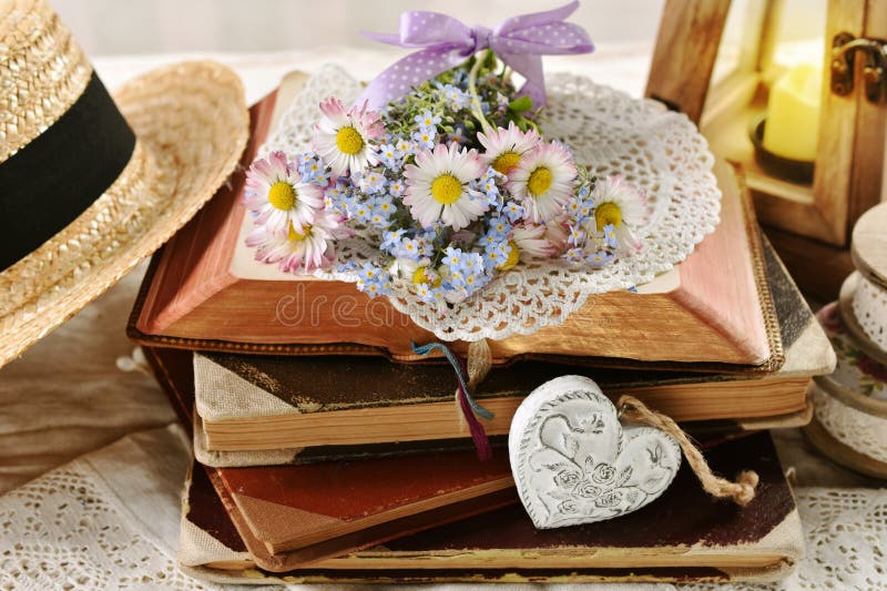 A small bunch of daisy and forget-me-not flowers lying on a stack of opened old books in vintage style interior. A small bunch of daisy and forget-me-not flowers lying on a stack of opened old books in vintage style interior
