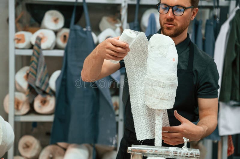 Man in Glasses and with Notepad is in the Room with Sewing Machines