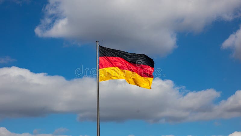 Bandeira alemão que acena em um mastro de bandeira contra o céu azul com nuvens, imagem de stock Bandeira alemão que acena em um mastro de bandeira contra o céu azul com nuvens, imagem de stock
