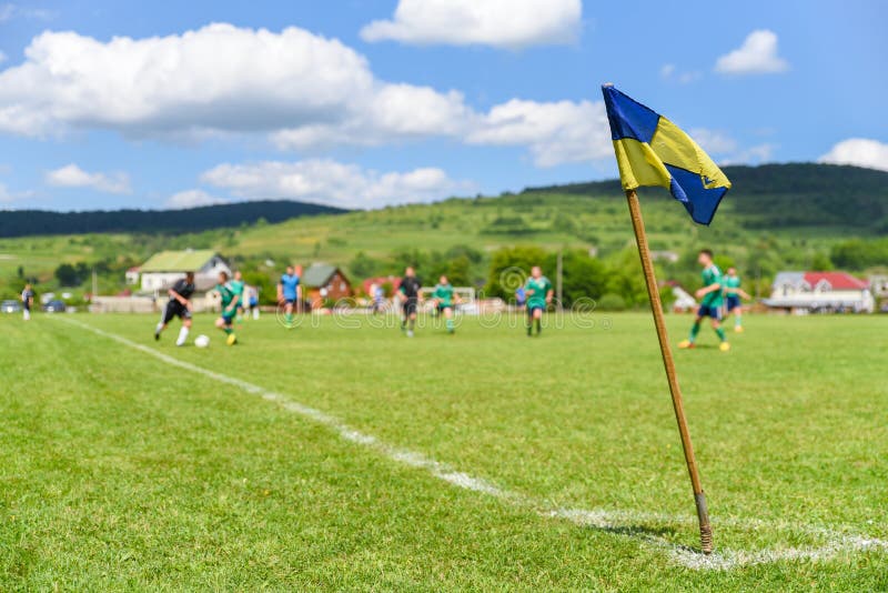 A bandeira de canto retro no primeiro plano do campo de futebol amador, no fundo obscuro é jogadores de futebol que lutam pela bo imagem de stock A bandeira de canto retro no primeiro plano do campo de futebol amador, no fundo obscuro é jogadores de futebol que lutam pela bo imagem de stock