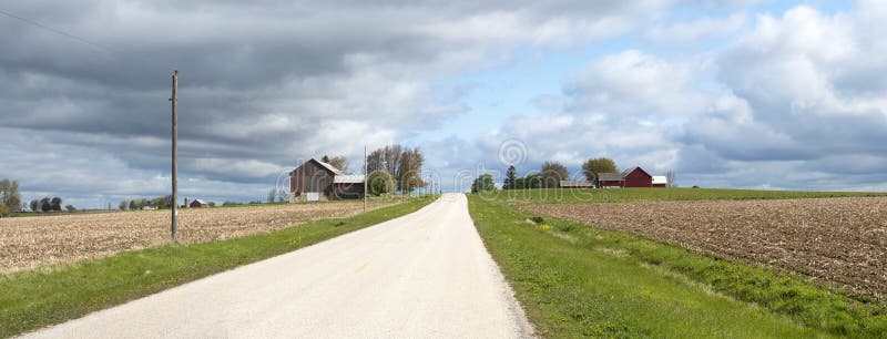 Old Wisconsin dairy farm and rural country road. Barns and fields can be seen in the image. Several images are stitched together to create a panorama or panoramic banner. Storm and stormy clouds in the sky are in the distance. Old Wisconsin dairy farm and rural country road. Barns and fields can be seen in the image. Several images are stitched together to create a panorama or panoramic banner. Storm and stormy clouds in the sky are in the distance.