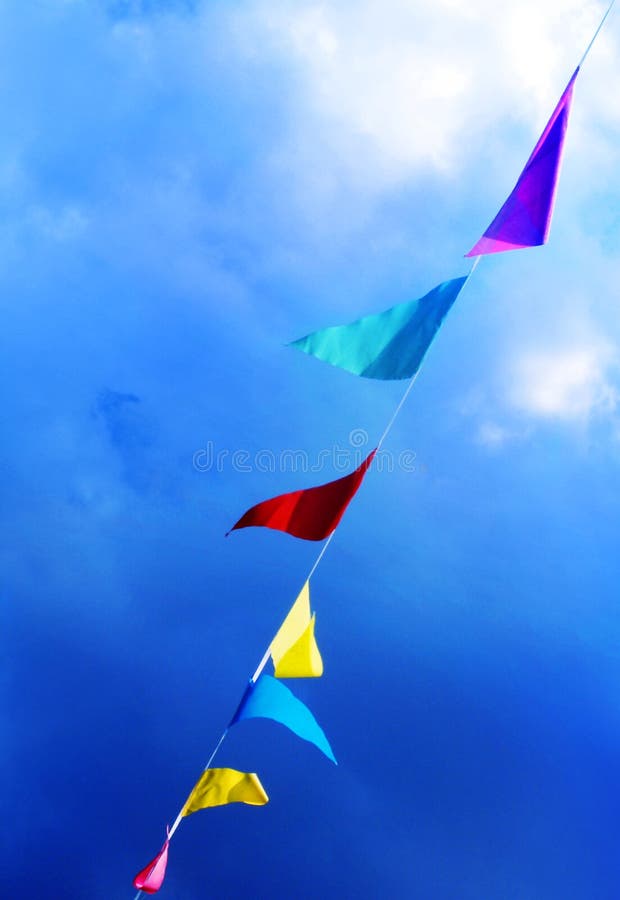 A string of colourful flags blowing in the wind under a bright blue sky. Diagonal composition for feeling of vibrance and energy. Vertical format. A string of colourful flags blowing in the wind under a bright blue sky. Diagonal composition for feeling of vibrance and energy. Vertical format.