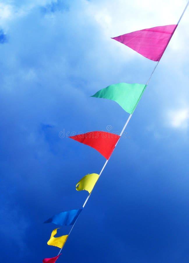 A string of brightly colourful flags blowing in the wind under a bright blue sky. Diagonal composition for feeling of vibrance and energy. Vertical format. Green energy source metaphor. A string of brightly colourful flags blowing in the wind under a bright blue sky. Diagonal composition for feeling of vibrance and energy. Vertical format. Green energy source metaphor.